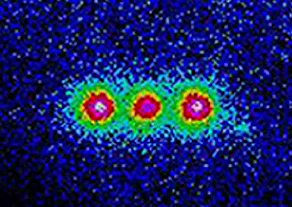 Three beryllium ions held in a trap at NIST, glowing under an ultraviolet laser, in a colorized image of 2005; kept apart from everything else, they can serve as qubits